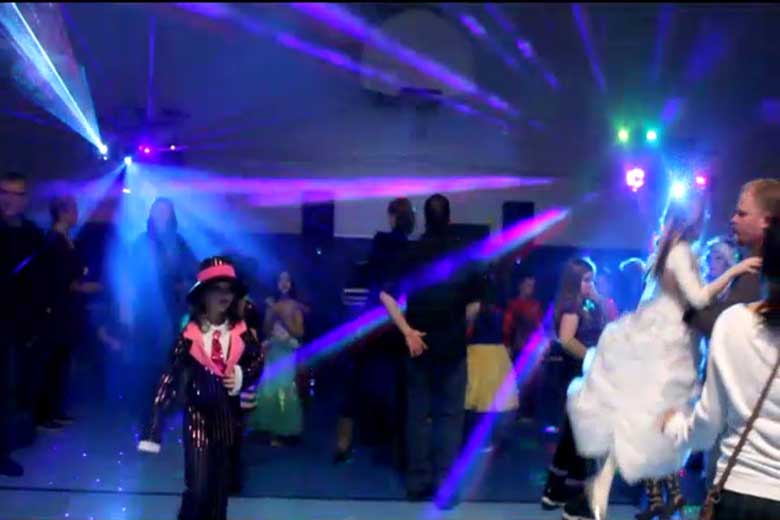 School Light Show, DJ Hamilton, Family Dance, guests dancing with laser beams & special  effects beams  everywhere, Blue beams of light fill the gym with a bit of pink & Green on the right. young girl dressed in a costume, black sparkly suit with top hat. Sparkly red tie. Hat has a pink band around it. White shirt under jacket. Taken in Hamilton.